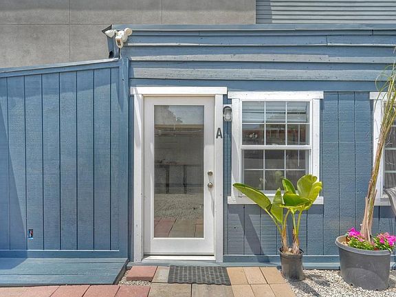 Detail of the front entrance to Unit A: a white-framed door marked with a letter A, a security floodlight above, a divided-light window beside it, and a banana plant in a terracotta pot at the threshold