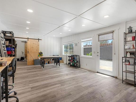Interior of one studio unit currently used as a workshop: light wood-look flooring, white walls, drop ceiling with recessed lighting, a sliding barn door, and a long workbench along the left wall
